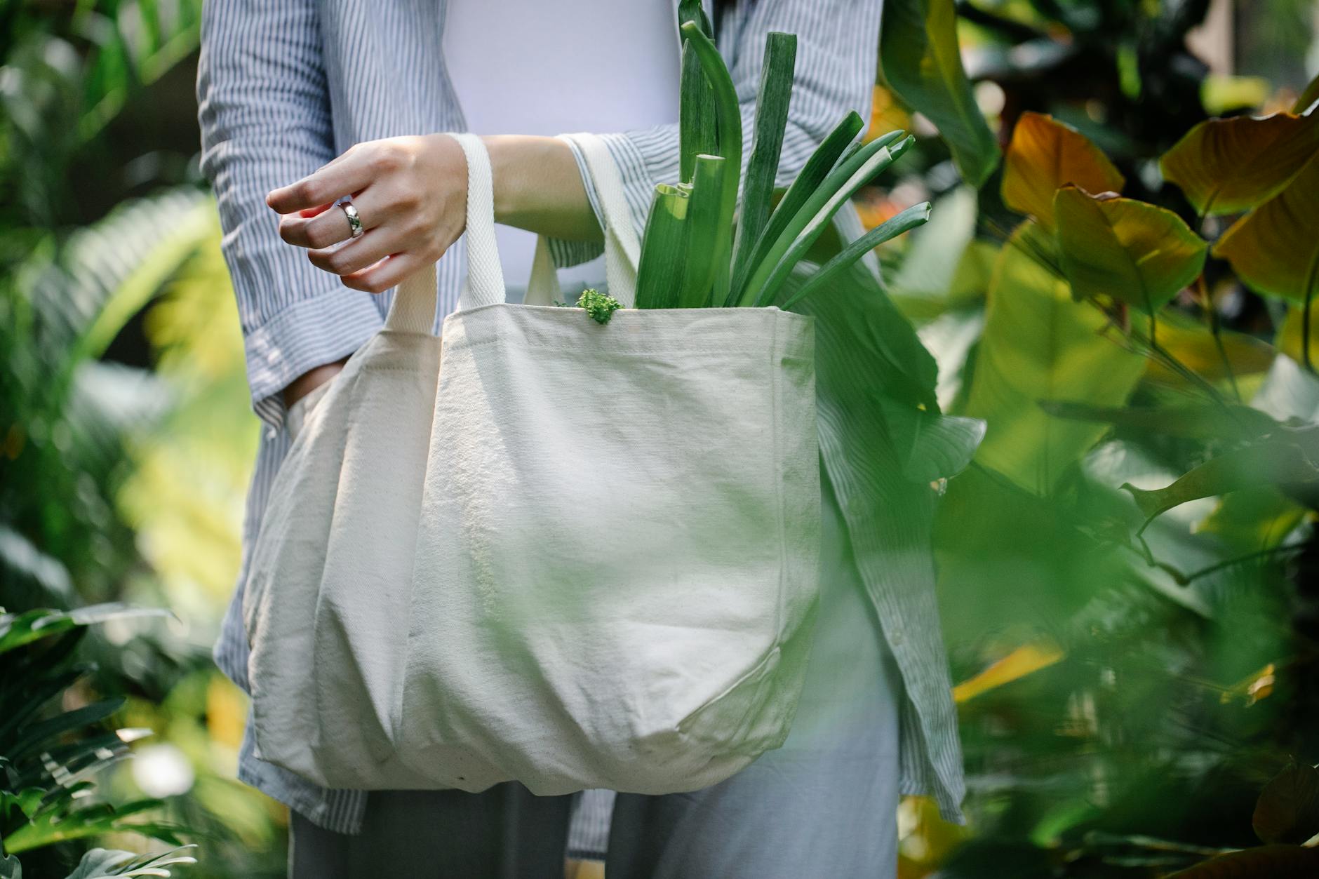 woman with shopper with products walking among green plants